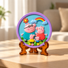 Round DIY pig family painting craft with four pink cartoon pigs, rainbow, clouds and purple border displayed on a table top stand.