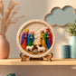 Colourful round Nativity scene craft featuring baby Jesus, four figures and two sheep on a display stand.