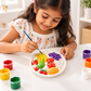Little girl painting a DIY fruit craft plaque with bananas, grapes, apples, pear and watermelon using colourful paints.