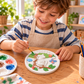 Child painting a round monkey tree DIY craft plaque with brush and colourful paints