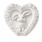 A white heart-shaped decorative plaque featuring a sculpted bunny in the centre, surrounded by a border of roses and daisies.