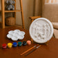 Unpainted round Nativity scene DIY craft displayed with paint pots, palette and brushes.